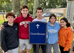 A group of teenage volunteers in front of the Cushing Greenhouse sign