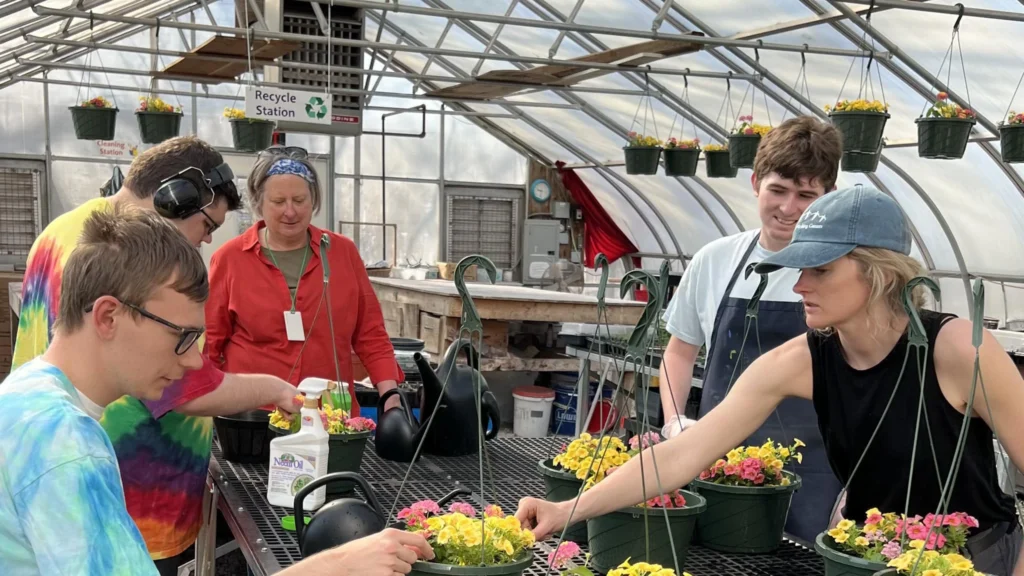 Group of students and teachers in greenhouse tending flowers. 