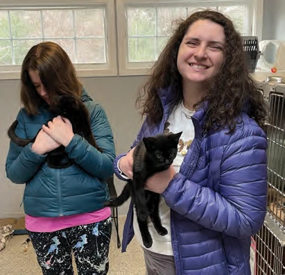 Cory Milton and Emma Sage holding black cats at the Scituate Animal Shelter.