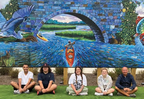 Students Nick Frazier and Vinny Johnson, art teacher Emily McElman, student Ainsley DiTomaso and manager of art enrichment Randy Wiskow with their new mural of kayakers at Hanover Crossing.