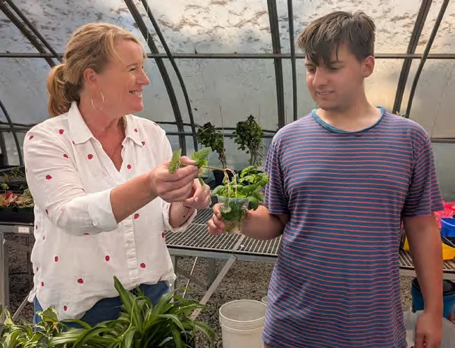 Owen Putlack shows President and CEO Michelle Markowitz plants in the greenhouse.